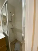 Shower in the Interior Apartment bathroom with sliding glass screen and a folded grey towel on the floor